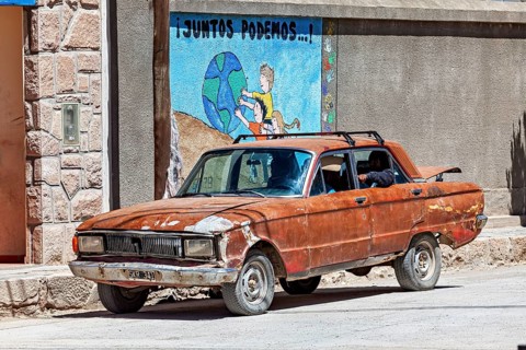 A rusty car stands on a dusty road in front of a colorful mural, Old car in traffic in San Antonio