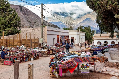 A marketplace with colorful fabrics and stalls in front of a majestic mountain landscape, tourist