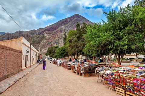 A market with colorful fabrics along a street nestled in a mountainous landscape, tourist and