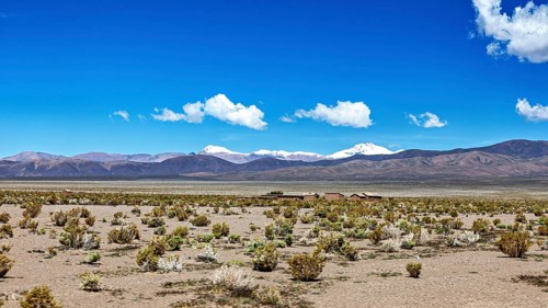 Wide desert landscape with snow-covered mountains under blue sky and scattered clouds, The