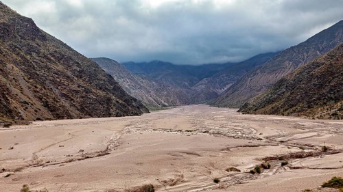 Wide valley between two dark mountain ranges under a cloudy sky, the landscape and colorful rock
