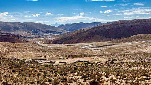 Wide plain with few shrubs, surrounded by barren desert and mountains, the landscape and colorful