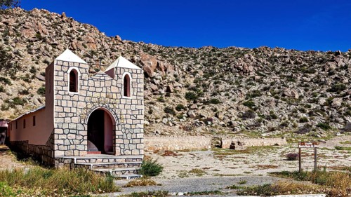 Small chapel in a wide desert landscape with rocky surroundings under bright blue sky, The chapel