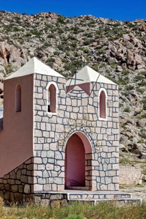 Small stone chapel in a remote desert landscape against a rocky backdrop under a blue sky, The