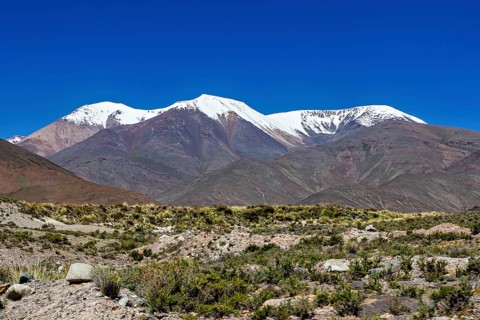 Snowy mountains tower over a barren desert landscape under clear skies, roads through the landscape
