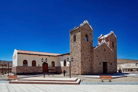 Stone church with two towers under clear blue sky in an open square with lanterns, Parroquia San