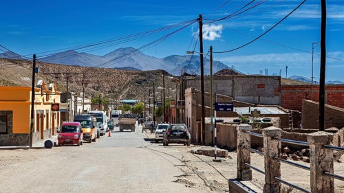 Several cars in a hilly desert town surrounded by mountains under blue skies, San Antonio de los