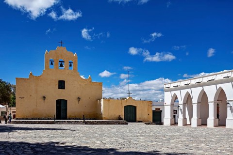 Yellow church with bell tower in front of a large square under bright blue sky, Iglesia San José de