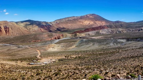 View of barren desert landscape with hills and mountains under clear skies, roads through the