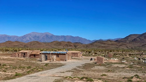 Cabins in an open desert landscape with dry soil and mountains in the background, San Antonio de