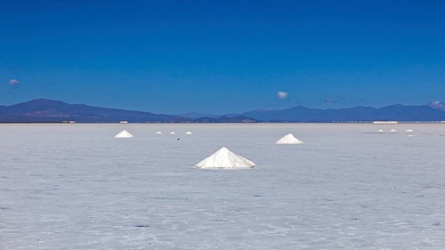 Wide salt desert with salt formations in the foreground and mountains on the horizon under clear