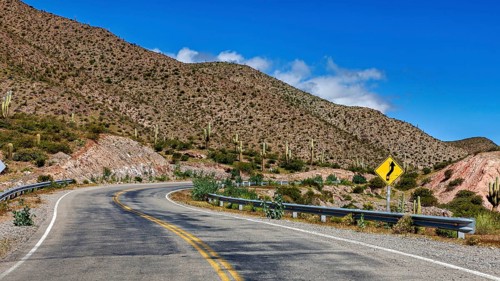 Winding road through mountain landscape with cacti and sky, The landscape of the Quebrada with its