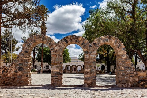 Stone arches on a sunny square with trees and partly cloudy sky, Downtown Cachi in Argentina