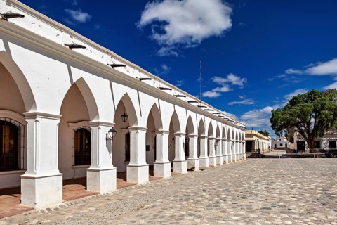 Arcades along a paved square in sunny weather with blue skies and trees, The arcades of Cachi in