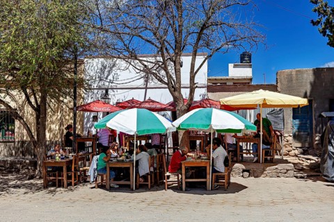 Outdoor area with dining tables and colorful umbrellas where people sit in the shade in sunny