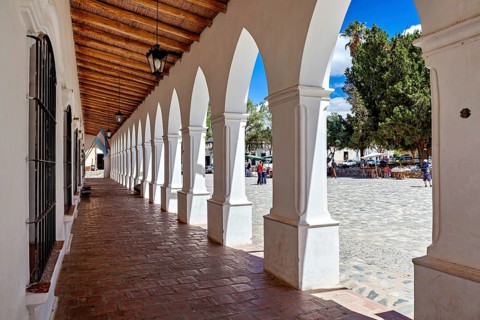 Long arcade with wooden ceiling, combines interior with a sunny square, The arcades of Cachi in