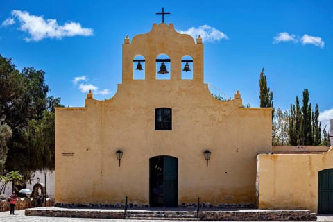 Front view of a yellow church with bells and cross under a blue sky, Iglesia San José de Cachi in