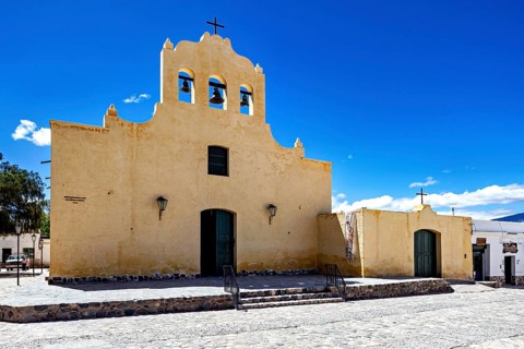 Yellow church with bell tower and cross against a clear sky, colonial style of architecture,