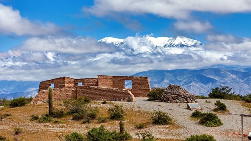 Old stone ruin in a desert-like landscape with mountains in the background and snow-capped peaks,