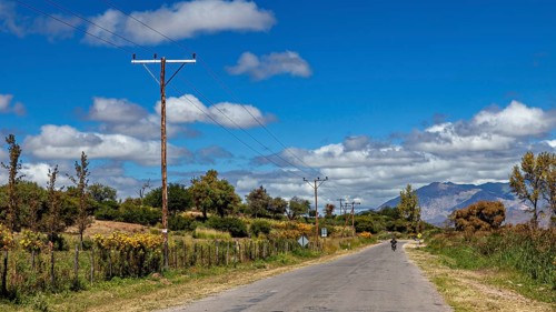 Rural road with electricity poles and trees under a cloudy blue sky, roads through the Quebrada de