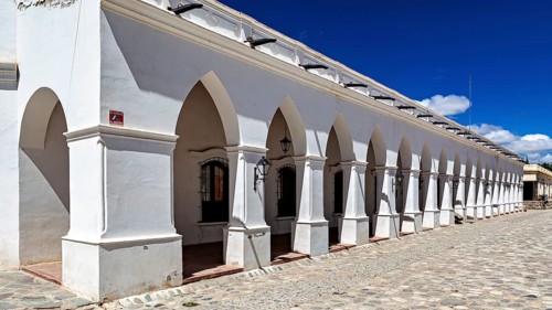 White building with colonial-style arcades under clear blue sky, The arcades of Cachi in Argentina