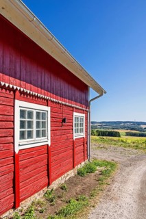 Red wooden rural barn beside a gravel road with a scenic landscape view in the countryside a sunny
