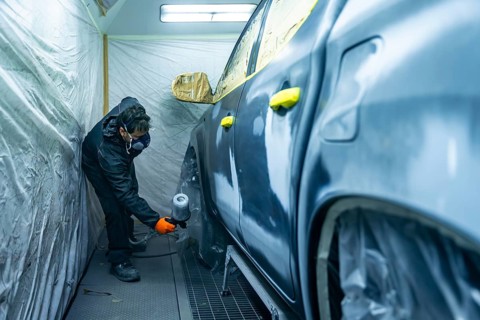 Auto body technician working in a repair shop, carefully applying paint primer to a vehicle door