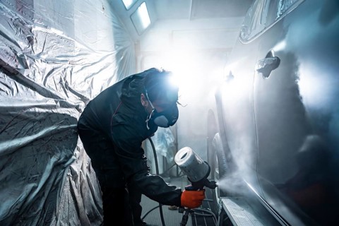 Auto body painter wearing a respirator mask and protective suit, carefully applying a fresh coat of