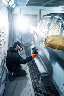 Professional auto body mechanic kneeling while applying primer or paint to a passenger cars side