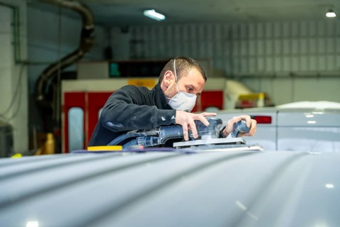 Auto body technician wearing protective mask sanding a vehicle roof with an orbital sander at a