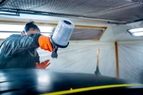 Automotive technician wearing safety gloves and mask meticulously applying a fresh coat of paint to