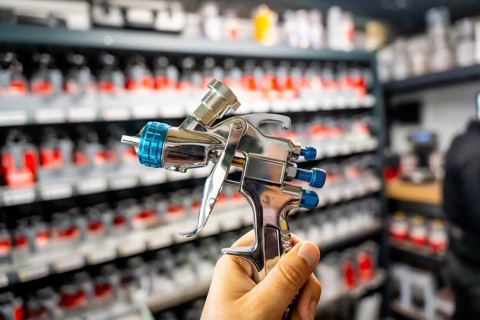Hand holding a high pressure spray gun, selecting paint colors from shelves in an automotive