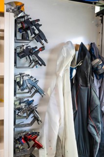 Modern spray guns and protective gear, including a disposable suit and a respirator mask, hanging