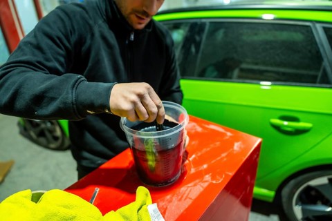 Male worker preparing automotive paint in a plastic container with a lime green vehicle visible in