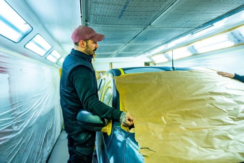 Skilled technician carefully masking vehicle with brown paper and tape, preparing it for a