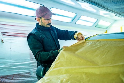 Auto body technician carefully applying masking paper and tape to a vehicle in a professional car