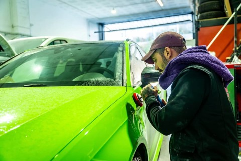 Auto body technician working on a vibrant green car, using a polisher to refine and enhance the