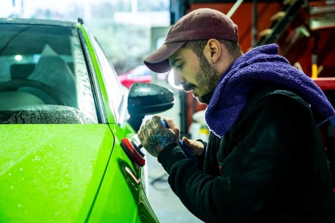 Man polishing a bright lime green car with a buffer in an auto body shop, applying a fine finish