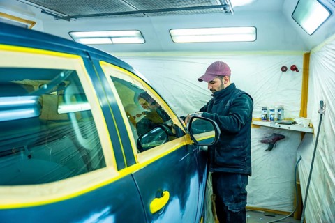 Auto repair technician carefully applying masking tape to a car door and window, protecting parts