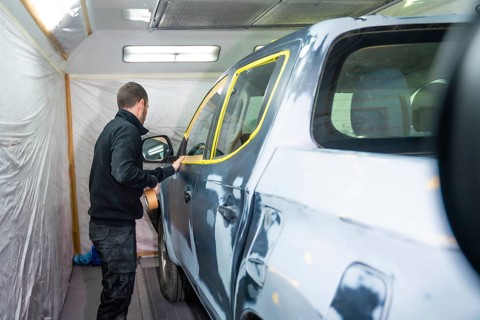 Mechanic applying masking tape to a car surface, meticulously preparing the vehicle for a fresh