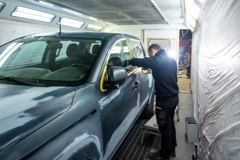 Automotive technician preparing a vehicle for painting by carefully applying protective masking