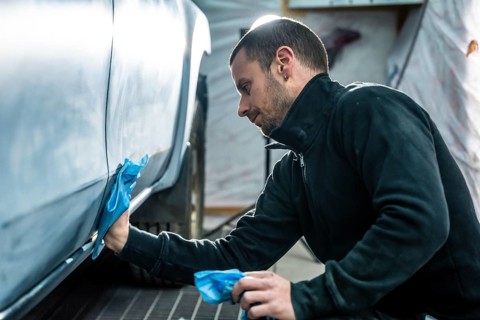 Focused mechanic carefully smooths and cleans car body surface before painting inside a modern auto