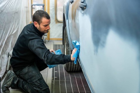 Auto body technician in a workshop cleaning and preparing a car door for painting with a microfibre