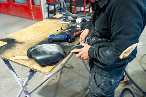Auto body repairman meticulously sanding a car part, preparing surfaces for paint spraying,