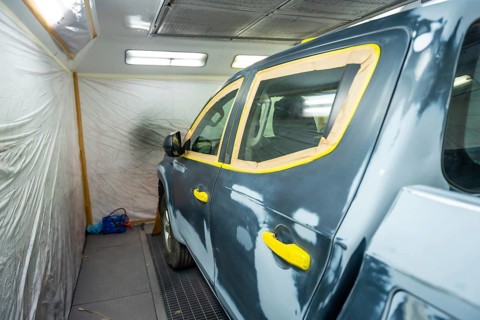 Vehicle in a body shop prepped for painting, masked with tape over windows and trim, primed and