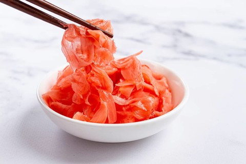 Pickled ginger, with chopsticks, in a small white bowl, on a marble countertop, close-up, no people