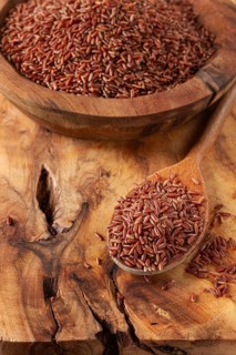 Natural, red rice, in a wooden bowl and spoon on a wooden surface in rustic style, top view