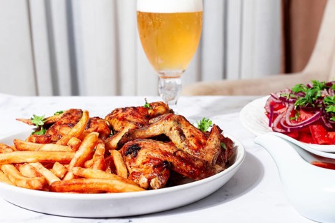 Delicious barbecue chicken wings, with French fries, salad and a refreshing drink, at a cozy table,