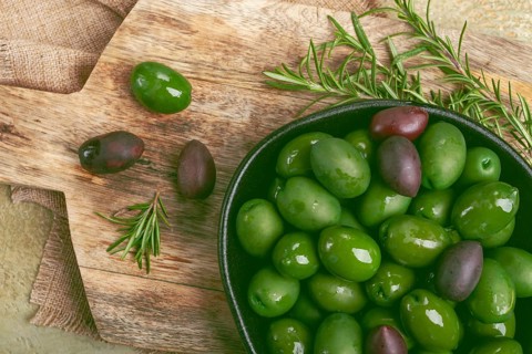 Chalkidiki olives, classic Greek green olives, in a bowl on a cutting board, top view, without