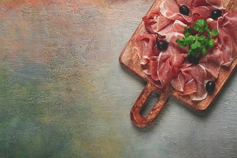 Sliced prosciutto, on a cutting board, with olives and herbs, snack, breakfast, no people